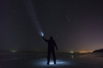 Russie, oblast d'Amour, silhouette de l'homme aux rayons bleus debout sur la rivière Zeya gelée la nuit sous le ciel étoilé — Photo de stock