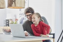 Pai feliz e filha usando laptop na mesa em casa — Fotografia de Stock