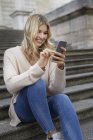 Portrait of happy young woman sitting on stairs using smartphone — Stock Photo