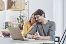 Smiling couple with a card using laptop on table at home — Stock Photo
