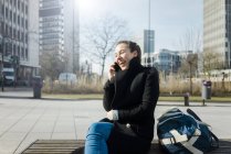 Allemagne, Essen, jeune femme riante au téléphone assise sur un banc à l'extérieur — Photo de stock