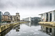 Germania, Berlino, Berlino-Mitte, distretto governativo, Reichstag e Paul-Loebe-Building con il fiume Spree in primo piano in inverno — Foto stock