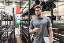 Man with clipboard on factory shop floor looking around — Stock Photo