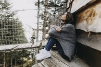 Mujer joven sentada en una casa de madera en la naturaleza relajante - foto de stock