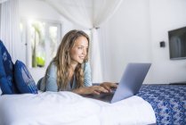 Mulher sorridente deitada na cama usando laptop — Fotografia de Stock