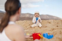 Счастливая девочка играет на пляже и смотрит на мать — стоковое фото