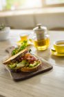 Pan crujiente con ensalada verde y jamón en plato de madera y té verde en la cafetería - foto de stock