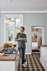 Человек с помощью планшета на кухне и глядя на потолочную лампу — стоковое фото