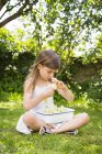 Bambina seduta sul prato in giardino con ciotola di fiori di sambuco raccolti — Foto stock