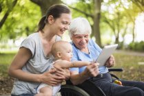 Avó, filha e neta se divertindo com tablet em um parque — Fotografia de Stock