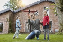 Padre con due bambini che giocano con l'aeroplano giocattolo nel giardino della loro casa — Foto stock