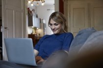 Portrait of smiling woman using laptop on couch at home — Stock Photo