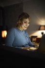 Портрет усміхнена жінка, використовуючи ноутбук вдома у вечірній час — стокове фото