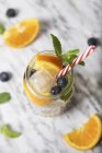 Glass of infused water with orange, blueberries and mint on ice — Stock Photo