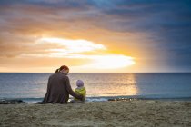Madre con figlioletta seduta sulla spiaggia al tramonto — Foto stock