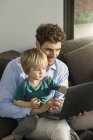 Father and son looking at laptop on couch at home — Stock Photo