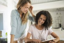 Deux femmes souriantes à la maison en utilisant une tablette — Photo de stock