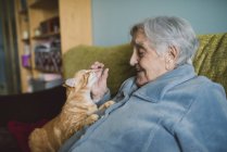 Glückliche Seniorin mit gestromter Katze auf der Couch — Stockfoto