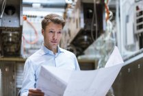 Businessman in factory holding plan — Stock Photo