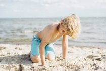 Biondo ragazzo giocare con sabbia su il spiaggia — Foto stock