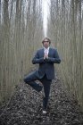 Uomo d'affari che pratica yoga tra i salici — Foto stock