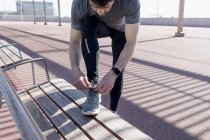 Homem esportivo amarrando seus sapatos em um banco — Fotografia de Stock