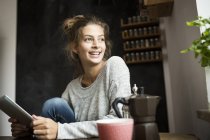 Mulher sorridente sentada à mesa e segurando comprimido — Fotografia de Stock