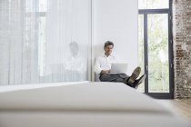 Empresario sentado en el banco en la oficina moderna y el uso de la computadora portátil - foto de stock