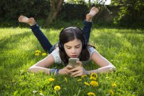 Girl lying on meadow listening music with headphones using smartphone — Stock Photo
