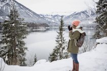 Giovane donna con bevanda calda in piedi nel paesaggio invernale alpino con lago — Foto stock