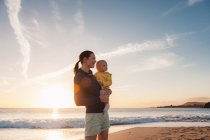 Madre che tiene la piccola figlia sulla spiaggia al tramonto — Foto stock