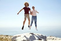 Sudáfrica, Ciudad del Cabo, feliz pareja joven saltando en la cima de la montaña en la costa - foto de stock