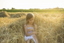 Petite fille assise sur la paille du champ possédé — Photo de stock
