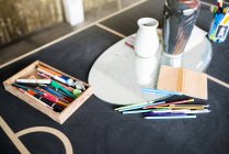 Lápices de colores, bolígrafos y un cuaderno sobre una mesa en el estudio del artista - foto de stock