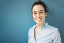 Ritratto di giovane donna sorridente che indossa occhiali davanti al muro blu — Foto stock