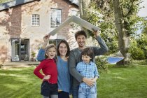 Portrait of happy family in garden of their home holding roof — Stock Photo