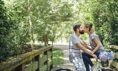 Couple à vélo embrassant sur une passerelle en bois à la campagne — Photo de stock