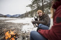 Couple on a trip in winter having a hot drink at camp fire — Stock Photo