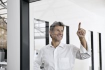 Smiling mature businessman touching glass pane in modern office — Stock Photo