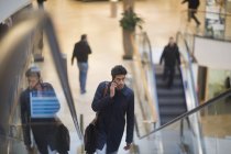Человек разговаривает по телефону стоя на эскалаторе в торговом центре — стоковое фото