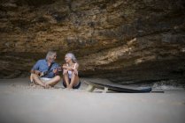 Beau couple âgé assis sur la plage, homme jouant de la guitare — Photo de stock