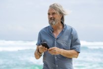 Красивий старший чоловік зі смартфоном на пляжі — стокове фото