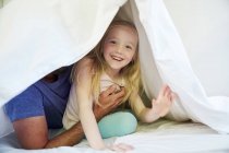 Ragazza felice con il padre seduto sul letto sotto coperta — Foto stock