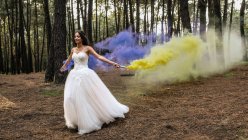 Mujer vistiendo vestido de novia en bosque sosteniendo antorchas de humo - foto de stock