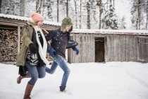 Coppia felice che corre davanti al mucchio di legna all'aperto in inverno — Foto stock