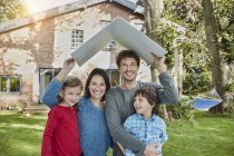 Portrait of happy family in garden of their home holding roof — Stock Photo