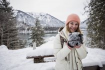 Young woman with hot drink standing in alpine winter landscape with lake — Stock Photo