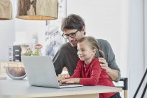 Sorrindo pai e filha usando laptop na mesa em casa — Fotografia de Stock