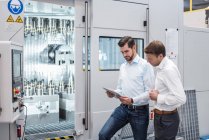 Dois homens em pé na máquina na fábrica olhando para tablet — Fotografia de Stock