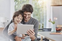 Feliz padre e hijo usando tableta en casa juntos - foto de stock